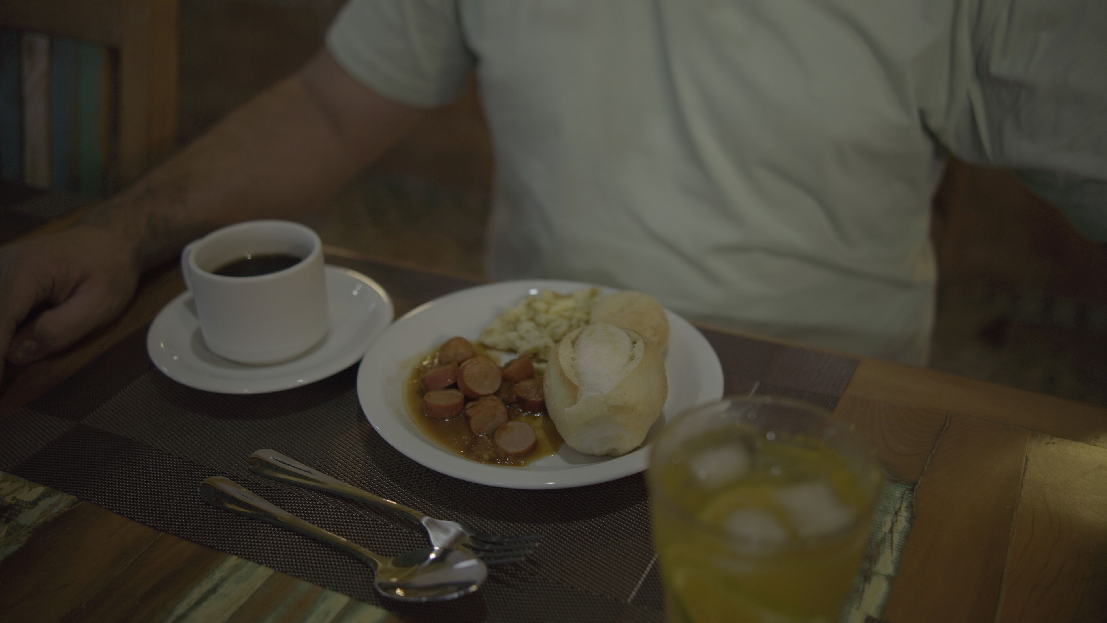 Una mesa de comedor con un plato de comida, una taza de café y un vaso de bebida.