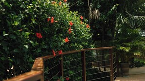 A wooden balcony railing with a view of lush green foliage and red flowers.