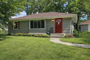 A single-story house with a red door, a small front porch, and a well-maintained lawn. - 4BR Near MOA & MSP | Game Room + Fenced Yard, Group Ready - Parking for 4 cars (Richfield)