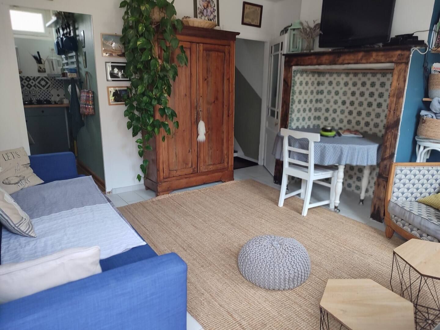 Een gezellige woonkamer met een blauwe bank, een houten kast en een eethoek met een witte stoel en tafel.