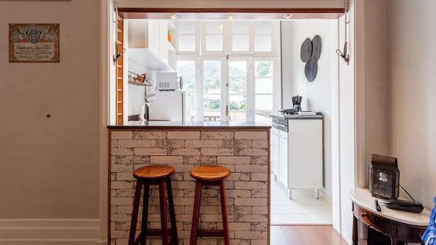 A kitchen with a brick accent wall, two wooden stools, and a view of the outdoor area.