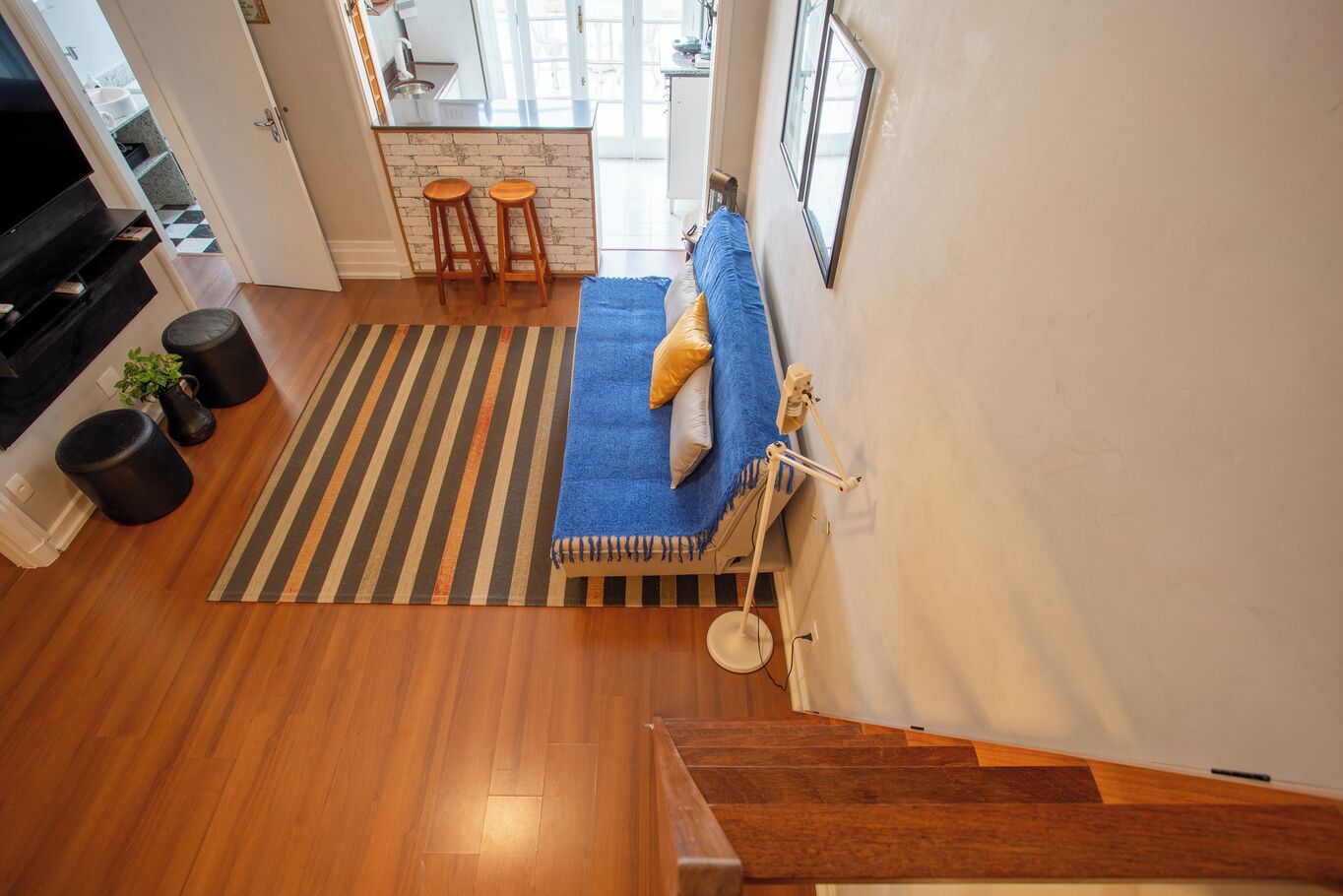 A modern living room with a wooden floor, a blue sofa, a striped rug, and a kitchen area in the background.