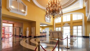 A spacious lobby with a grand chandelier, a reception desk, and a red rope barrier indicating a VIP area.