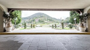 A view from under a covered area with potted plants on either side, leading to a paved area with a mountain in the background.