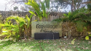 A sign reading "EcoVillage" with a stone wall and tropical plants in the background.