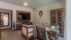A living room with a TV, wooden furniture, a dining table with chairs, and a cabinet with glass doors.