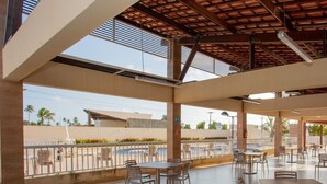 An outdoor cafe area with tables and chairs, a covered section, and a view of the surrounding landscape. - Apto com Piscina e Garagem em Barra dos Coqueiros (Barra dos Coqueiros)