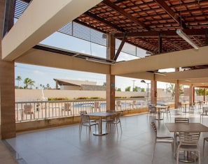 An outdoor cafe area with tables and chairs, a covered section, and a view of the surrounding landscape.