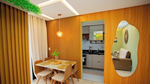 A modern kitchen with wooden paneling, a dining area with a table and chairs, and a living area with a sofa and a mirror. - Apto com Piscina e Garagem em Barra dos Coqueiros (Barra dos Coqueiros)