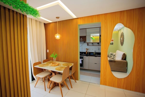 A modern kitchen with wooden paneling, a dining area with a table and chairs, and a living area with a sofa and a mirror.