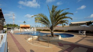 A swimming pool with a palm tree, lounge chairs, and a covered seating area. - Apto com Piscina e Garagem em Barra dos Coqueiros (Barra dos Coqueiros)