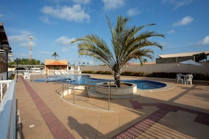 A swimming pool with a palm tree, lounge chairs, and a covered seating area.