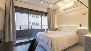 Ett modernt hotellrum med en säng, ett skrivbord och utsikt över staden genom stora fönster.