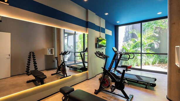 Ett gym med träningsutrustning, en stor spegel och utsikt över grönområden genom stora fönster.