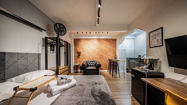 A modern hotel room with a bed, a desk, a chair, and a kitchen area. - Palacete Riachuelo (São Paulo)