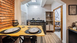 A compact kitchen with a brick wall, a dining area with a wooden table, and a view into the living space. - Palacete Riachuelo (São Paulo)