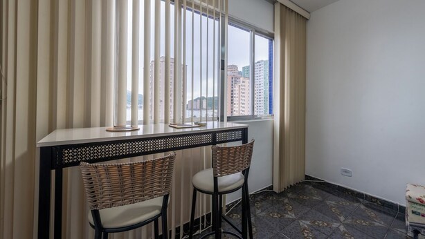 Una habitación con ventana, dos sillones de mimbre, una mesita y vistas a edificios altos.