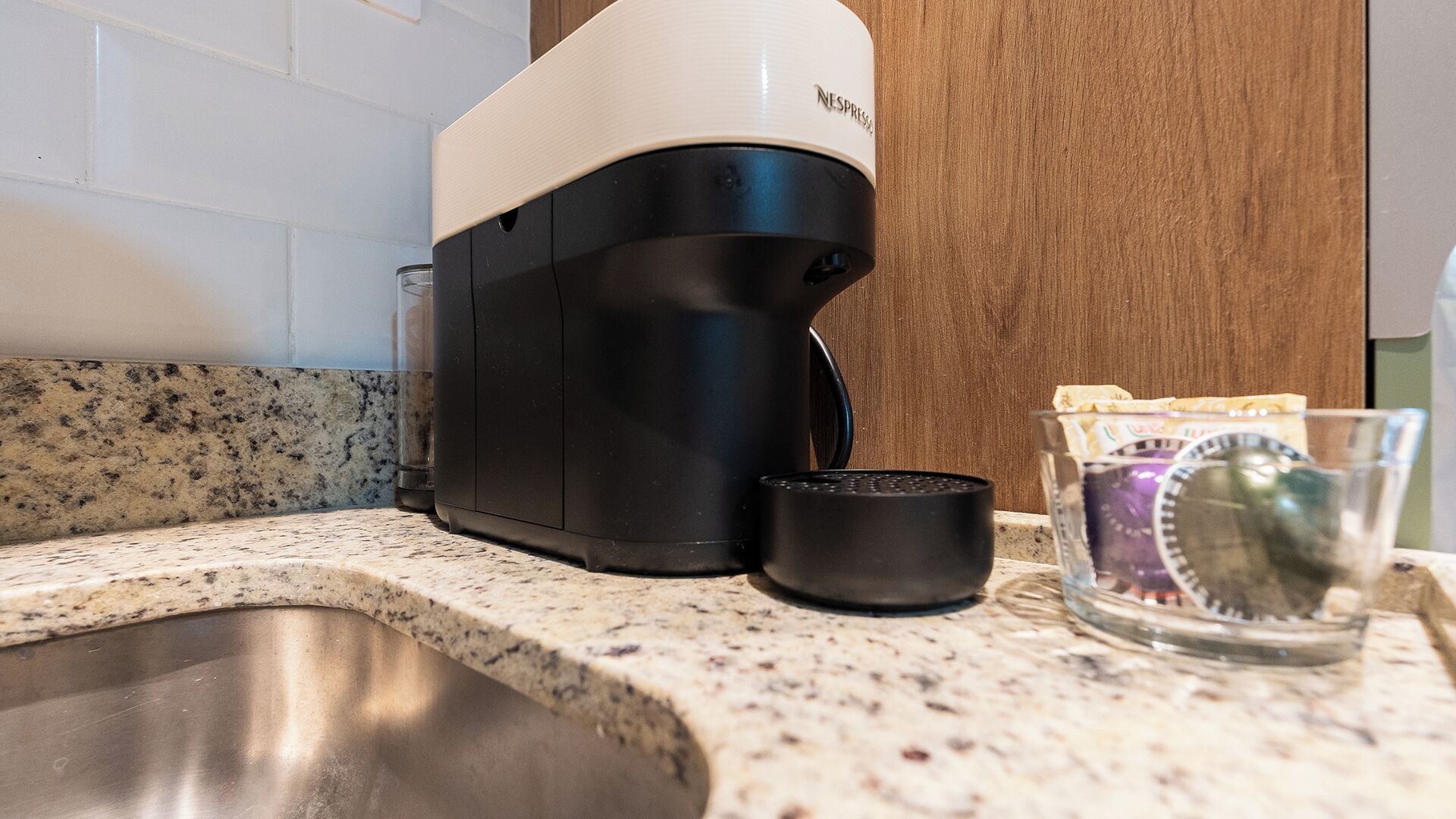 A kitchen with a coffee machine, a glass of water, and a packet of coffee pods on the counter.