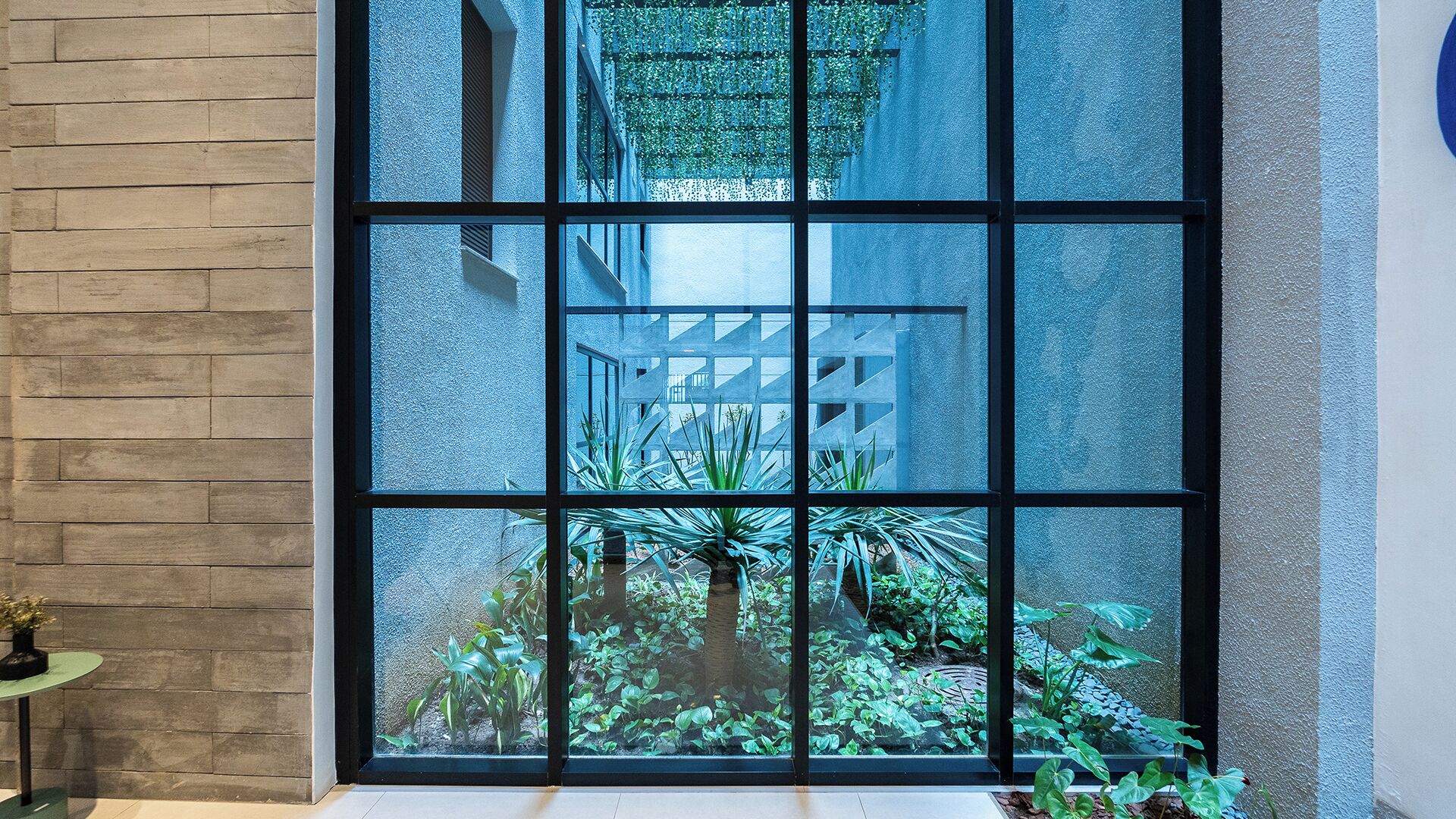 A window with a view of a building's interior, a brick wall, and a small table with a plant.