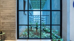 A window with a view of a building's interior, a brick wall, and a small table with a plant. - Think Santa Cecilia (São Paulo)