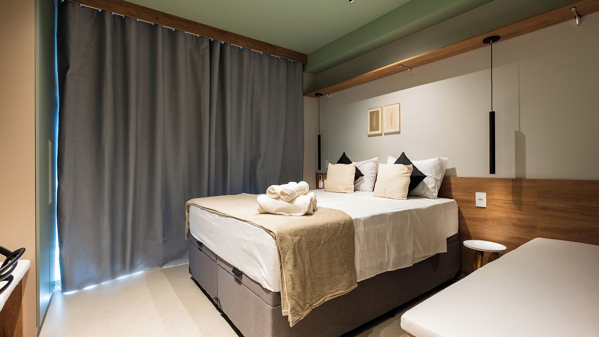 A modern hotel room with a large bed, a bedside table, and a small bedside table.