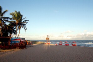 Una playa con una torre de salvavidas, palmeras y sombrillas rojas.