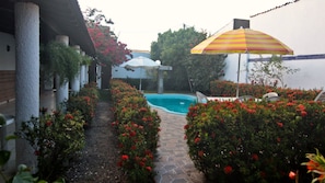 Piscina rodeada por un jardín con flores rojas y columnas blancas.