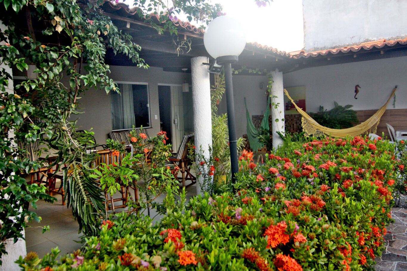Un espace patio aménagé avec des sièges d’extérieur, un hamac et une variété de plantes et de fleurs.