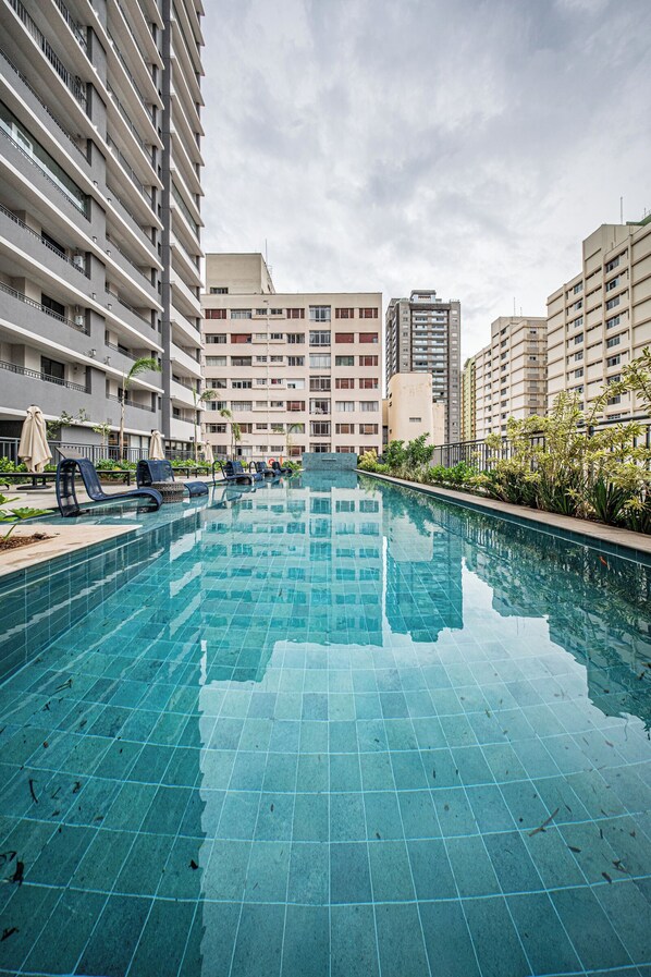 A swimming pool with lounge chairs and a view of high-rise buildings. - Nex One Paraiso (São Paulo)