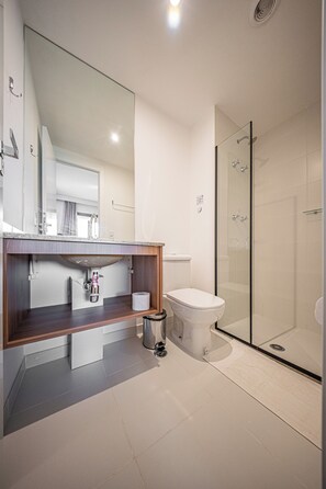 A modern bathroom with a wooden vanity, a toilet, a glass shower enclosure, and a large mirror. - Nex One Paraiso (São Paulo)