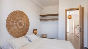 Een slaapkamer met een groot bed, een rond kunstwerk aan de muur, een houten plank, een rieten mand en een deur naar een badkamer.