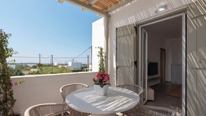 Een balkon met rieten stoelen, een ronde tafel en planten in potten.