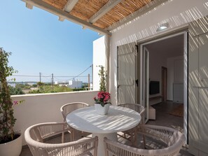 Ein Balkon mit Korbstühlen, einem runden Tisch und Blumentöpfen.