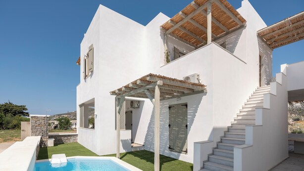 Een moderne witte villa met een zwembad, een stenen muur en een trap naar een hoger gelegen verdieping.