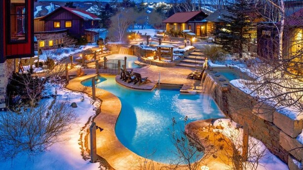 A resort with a large outdoor swimming pool, connected to a waterfall feature, surrounded by snow-covered grounds and illuminated by warm lighting. - Spacious Mountain-View Chalet | Walk to BM | Spa (The Blue Mountains)