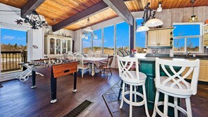 A spacious kitchen with wooden beams, a foosball table, and a large window offering a view of the outdoors. - Spacious Mountain-View Chalet | Walk to BM | Spa (The Blue Mountains)
