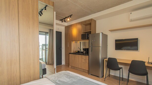Et moderne hotelværelse med seng, tekøkken, TV og skrivebord med stole.