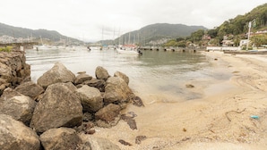 Eine felsige Küstenlinie mit Booten im Wasser, ein Sandstrand und Hügel im Hintergrund.