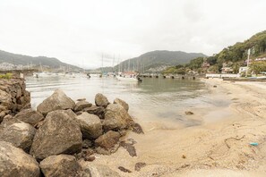 Eine felsige Küstenlinie mit Booten im Wasser, ein Sandstrand und Hügel im Hintergrund.