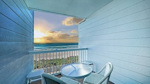 A balcony with a glass table and chairs, overlooking a beach with a sunset view. - Beachfront Condo w/ Pool & Gulf Views I Anna Maria Island I Seaside Beach Villa |   Steps to the Beach (Holmes Beach)