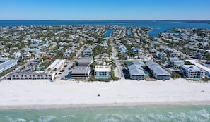 An aerial view of a coastal residential area with beachfront properties, a marina, and a bridge in the distance. - Beachfront Condo w/ Pool & Gulf Views I Anna Maria Island I Seaside Beach Villa |   Steps to the Beach (Holmes Beach)