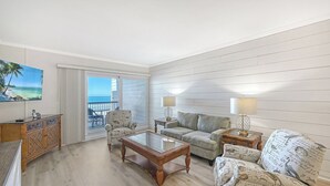 Ein Zimmer mit Balkon, Fernseher, Sofa, Couchtisch und zwei Lampen.