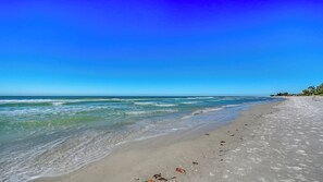 A beach with clear blue water, sandy shore, and a few scattered footprints. - Beachfront Condo w/ Pool & Gulf Views I Anna Maria Island I Seaside Beach Villa |   Steps to the Beach (Holmes Beach)
