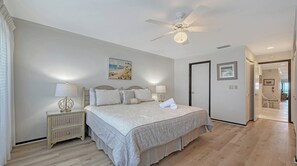 A bedroom with a bed, two bedside tables, a ceiling fan, and a door leading to another room. - Beachfront Condo w/ Pool & Gulf Views I Anna Maria Island I Seaside Beach Villa |   Steps to the Beach (Holmes Beach)