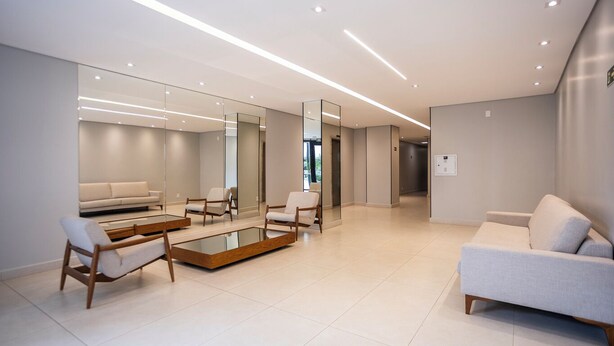 Um hall moderno e bem iluminado, com um sofá, cadeiras e uma mesa de centro de vidro.