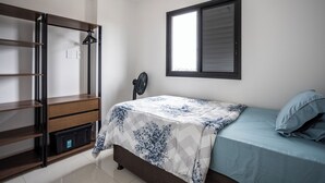Um quarto com uma cama, um guarda-roupa, uma janela e um ventilador.