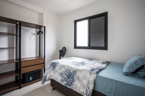 Un dormitorio con cama, armario, ventana y ventilador de pie.