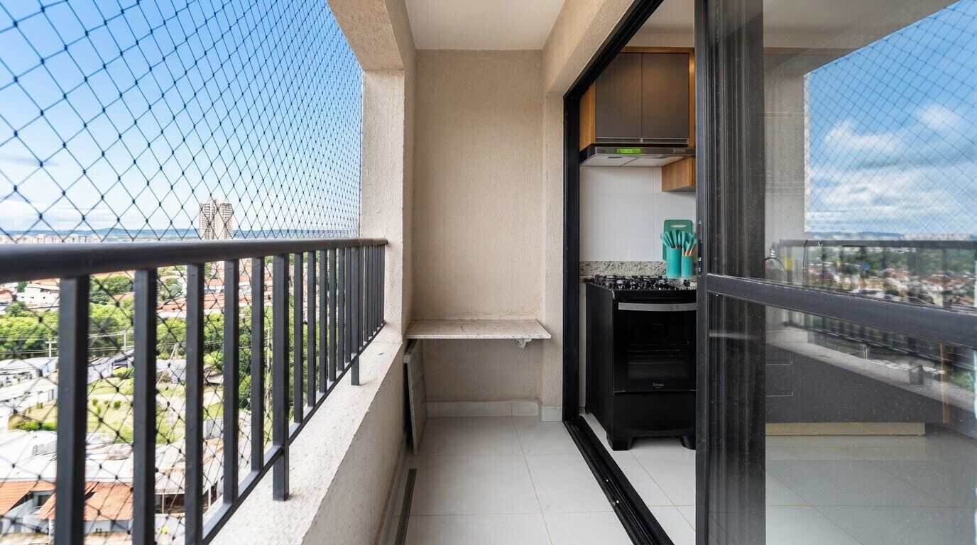 Un balcón con vistas a la ciudad, una cocina con estufa y armarios, y una puerta de cristal que da al interior.