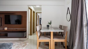 Uma sala de estar moderna com um rack de TV de madeira, uma mesa de jantar com cadeiras e uma cortina cinza.