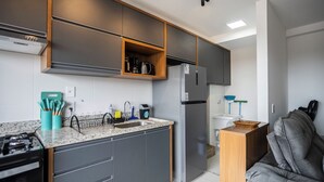 Cozinha moderna com armários cinza, forno embutido, geladeira e sofá cinza na sala de estar.